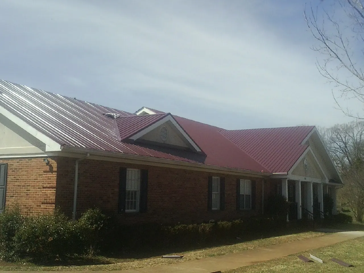 Red metal roof with gabled entries on a long brick building, from a Hail Damage Roof Repair job in Longford