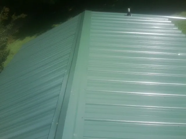 New green metal panels meeting at the ridge of a roof — Flat Roof Repair work by our crew in Longford
