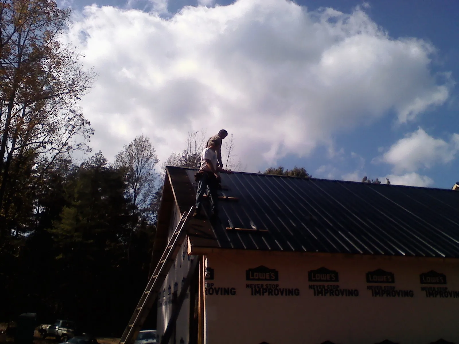 Roofer fastening dark metal panels high against a cloudy sky, from a Roof Inspection job in Longford