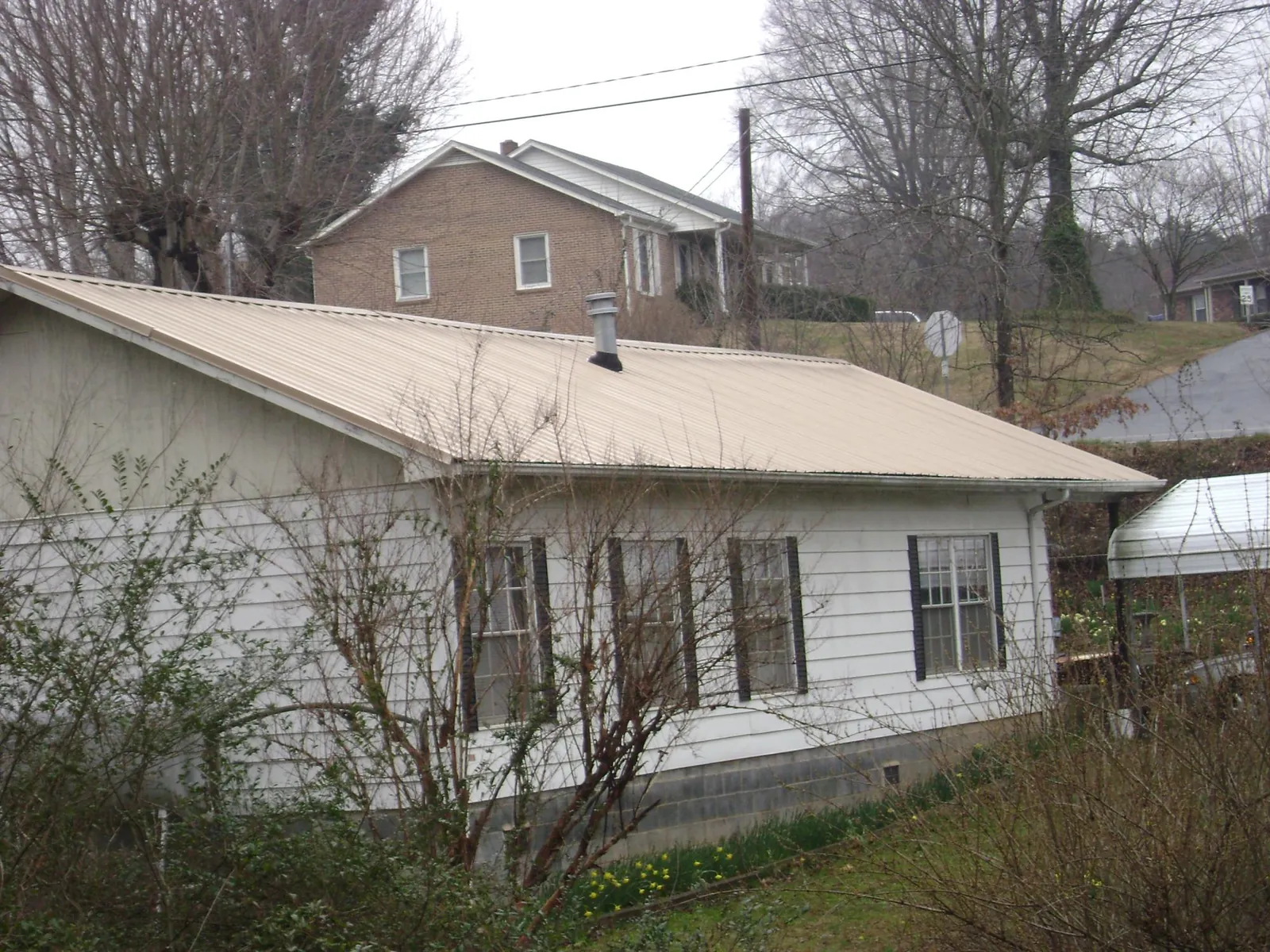 Tan metal roof on a white sided house set into a hillside — Commercial Roofing by Roofing Brothers in Longford