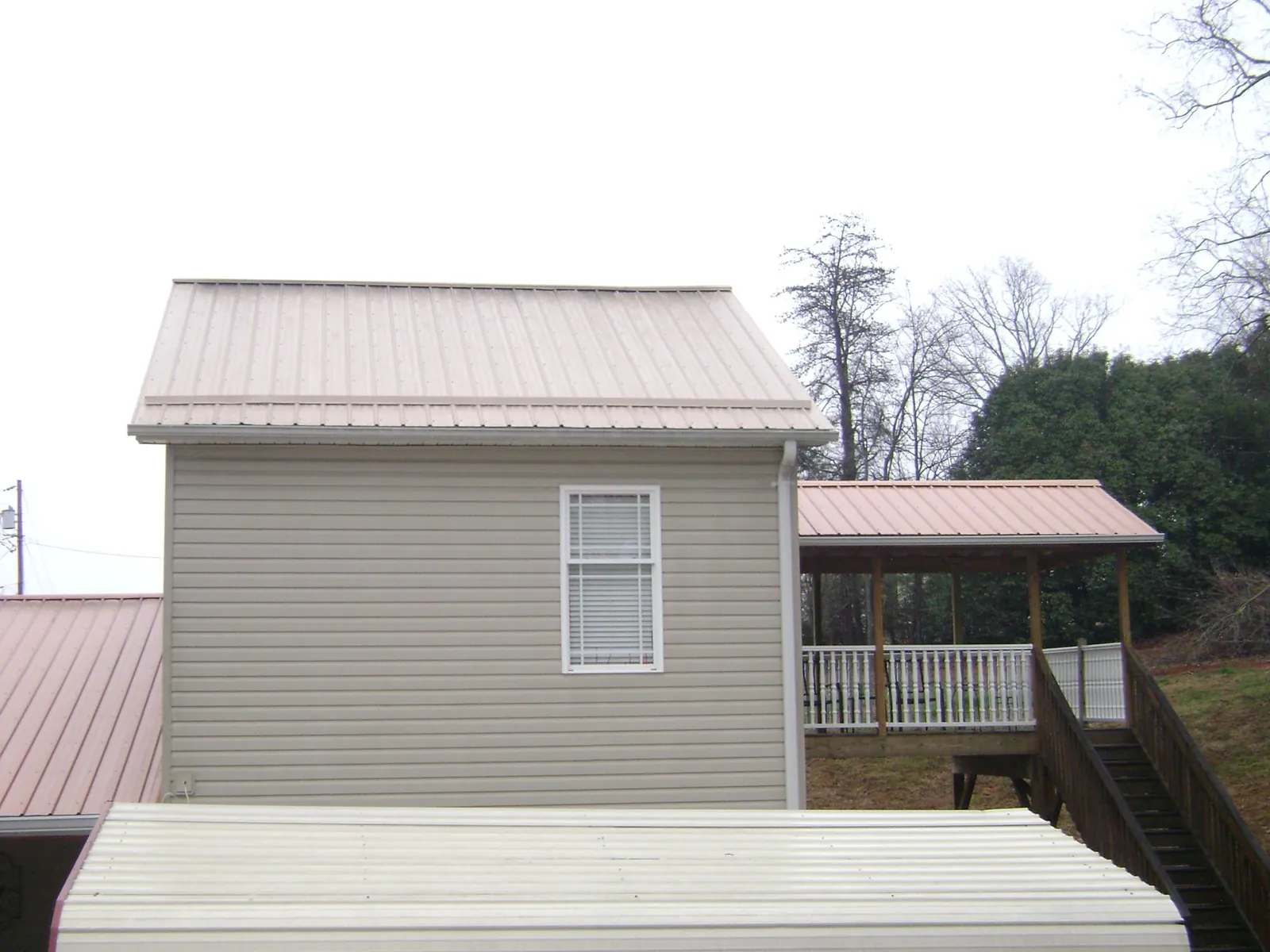 Tan metal roofs on a two story addition and attached porch, from a Roof Replacement job in Longford